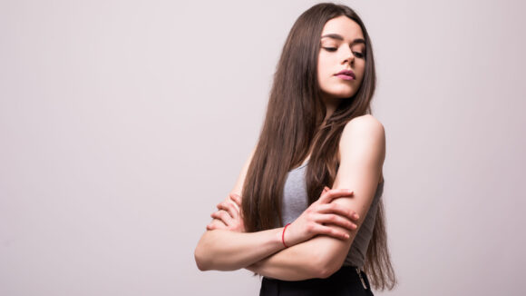 portrait of stylish young pretty woman smiling in grey t-shirt on white studio background, isolated, natural look, long brown hair, crossed arms